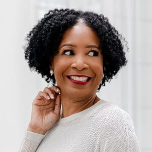 Headshot of Theresa M. Robinson looking off to the side, smiling, and dressed in white with red lipstick