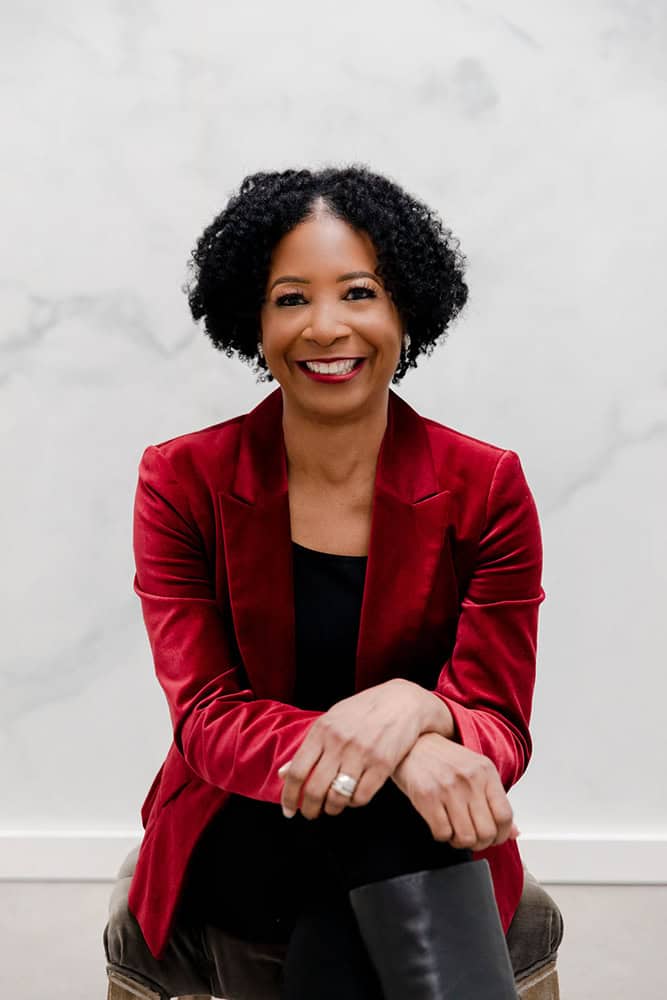 Theresa-M-Robinson-Well-Being-Leadership-DEI-Speaker-Facilitator seated with black boots and top with a dark red jacket