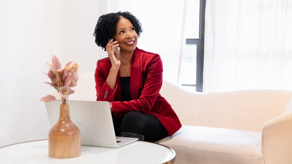 Theresa M. Robinson on a coaching call with laptop computer in front of her, and dressed in all black with a red jacket.